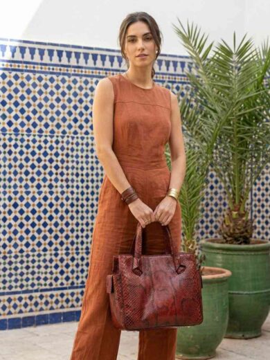 Handmade Kasba Leather Wildcard Bag in red anaconda serpent skin displayed on an artisan wooden desk.