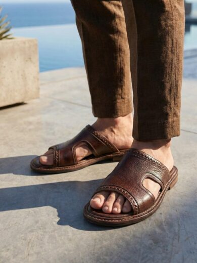 Top down view of handmade Men's Brown Leather Slides on a textured background.