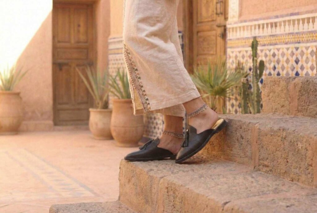 Woman wearing black leather Malika Babouche mules with tassel detail and silver anklets on Moroccan stone steps