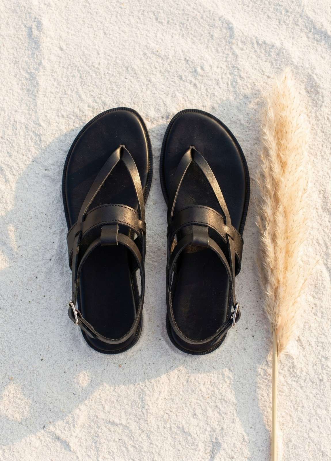Woman walking in handmade black leather T-strap flat sandals on white stone