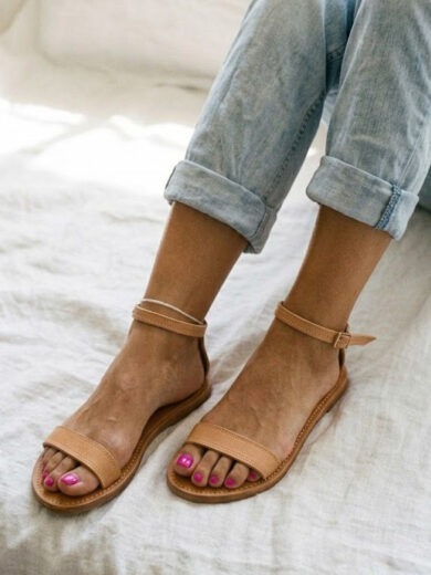 Woman wearing minimalist tan leather flat sandals with ankle strap — The Nadine by Kasba Leather
